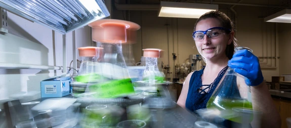 woman in lab, wearing goggles, holding lab beakers