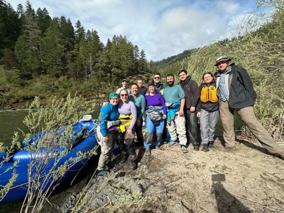 group of people standing on river bank, next to raft