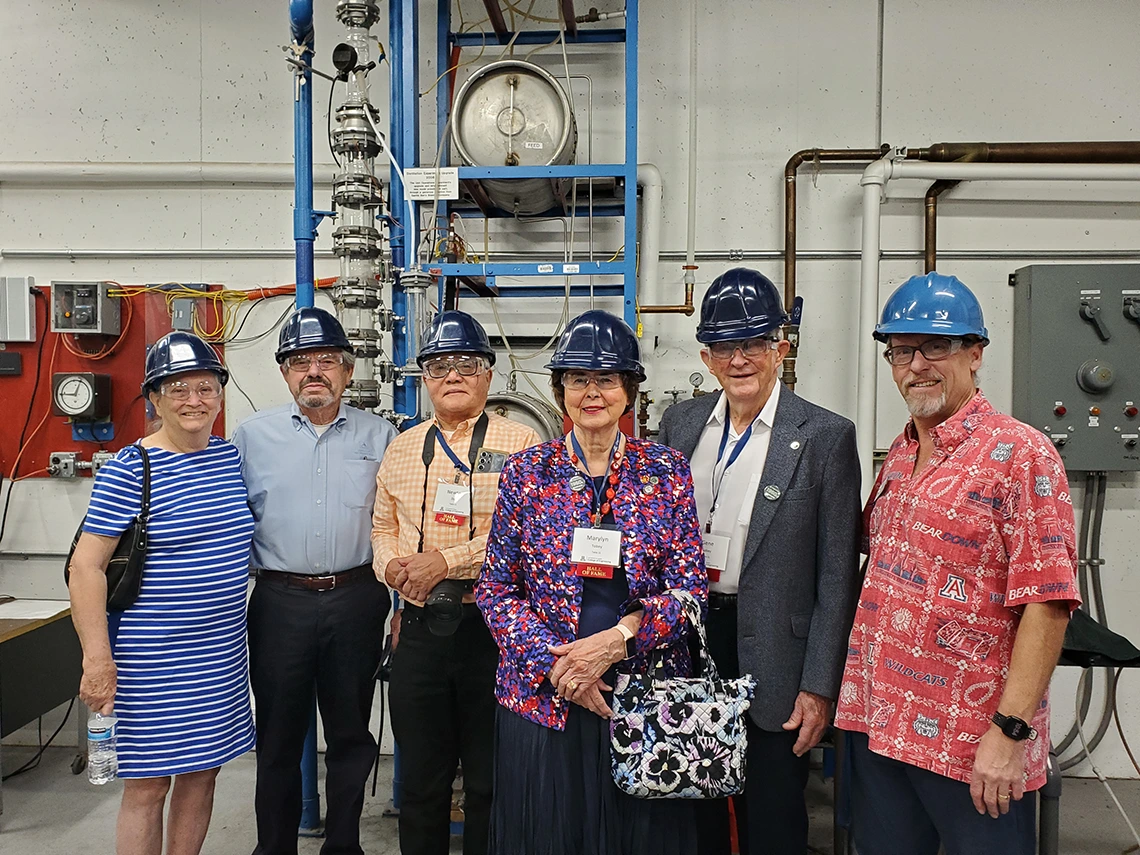 group of people wearing hard hats and safety goggle, standing in lab setting