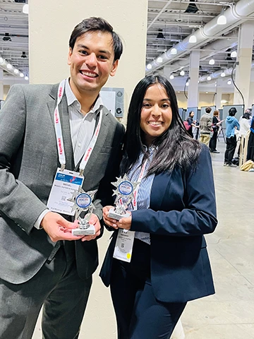 two people wearing business suits and lanyards, holding trophies