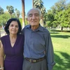 two people, standing and smiling, palm trees and grass in background