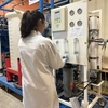 Researcher in white lab coat stands in front of water treatment equipment